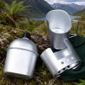 Canteen stove set with silver canteen, cup, stove body and green storage bag beside a lake and mountain view