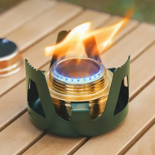 Alcohol stove burning with blue and yellow flame inside metal pot support on an outdoor table