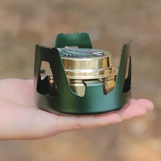 Compact alcohol stove with burner and pot support resting in a hand to show packed size