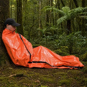 Person sitting in an orange survival bag in a bush setting