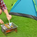 Compact hiking BBQ grill with glowing coals cooking food on grass