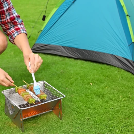 Compact hiking BBQ grill with glowing coals cooking food on grass