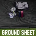 Black poncho tarp laid flat as a groundsheet with camping cookware and bag