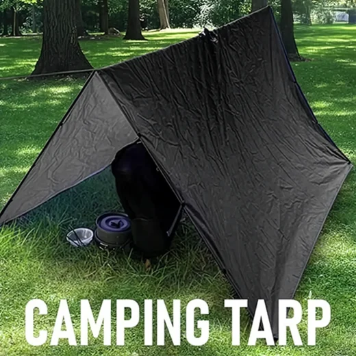 Black poncho tarp pitched as an A frame camping shelter over gear on grass