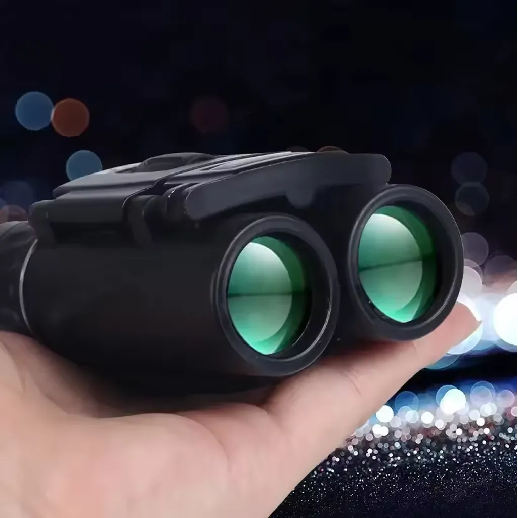 Mini binoculars resting on a hand with green coated front lenses, shown in low light to represent evening viewing and travel use