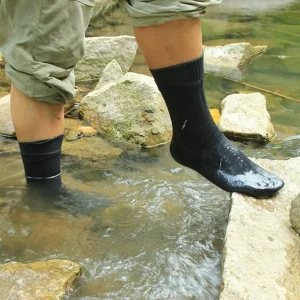 Person standing on rocks in a shallow stream wearing black waterproof socks