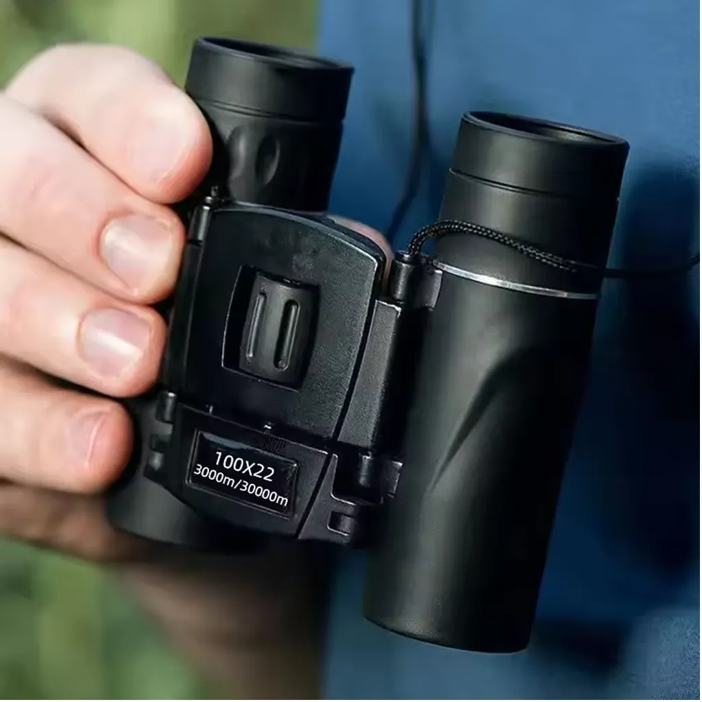 black mini binoculars held in one hand outdoors, showing the compact folding body and centre focus wheel for quick viewing