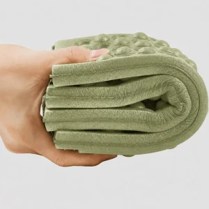 Army green folding outdoor seat pad compressed in one hand to show its flexible foam construction