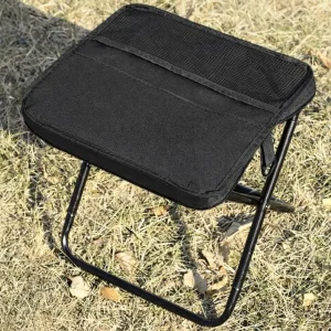 Black foldable stool set up outdoors on dry grass for camping, fishing, or picnic seating