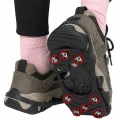 Black ice grips fitted over hiking shoes, showing eight traction studs beneath the raised sole