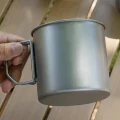 Hand holding a camping cup by its folding metal handle