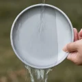 Metallic grey camping plate held upright while rinsing with water