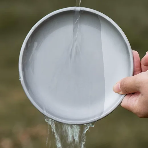 Metallic grey camping plate held upright while rinsing with water